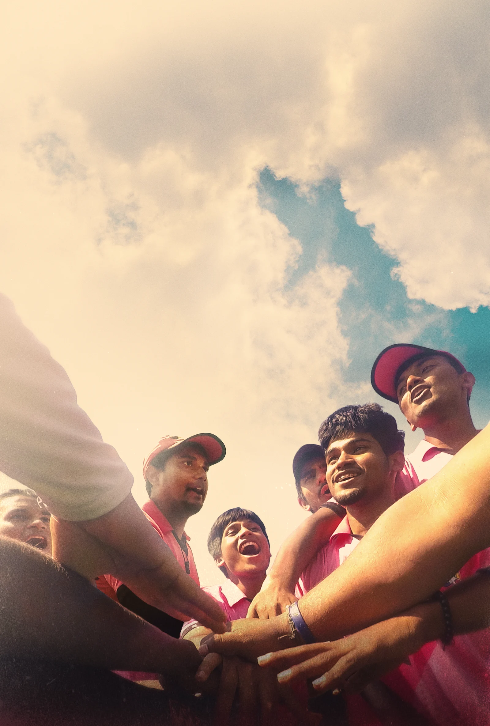 Chasing Cricket players join hands in a team huddle under a bright sky